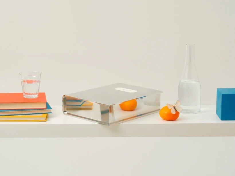 A shiny metal object in the shape of a book, on a shelf with everyday objects. Designed by Mario Tsai Studio 