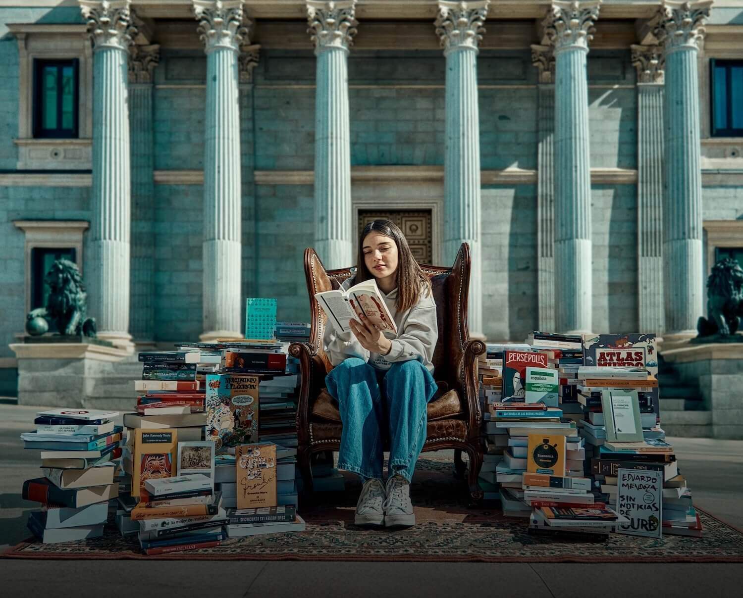 A young woman reading, in front of a government building, surrounded by stacks of books 