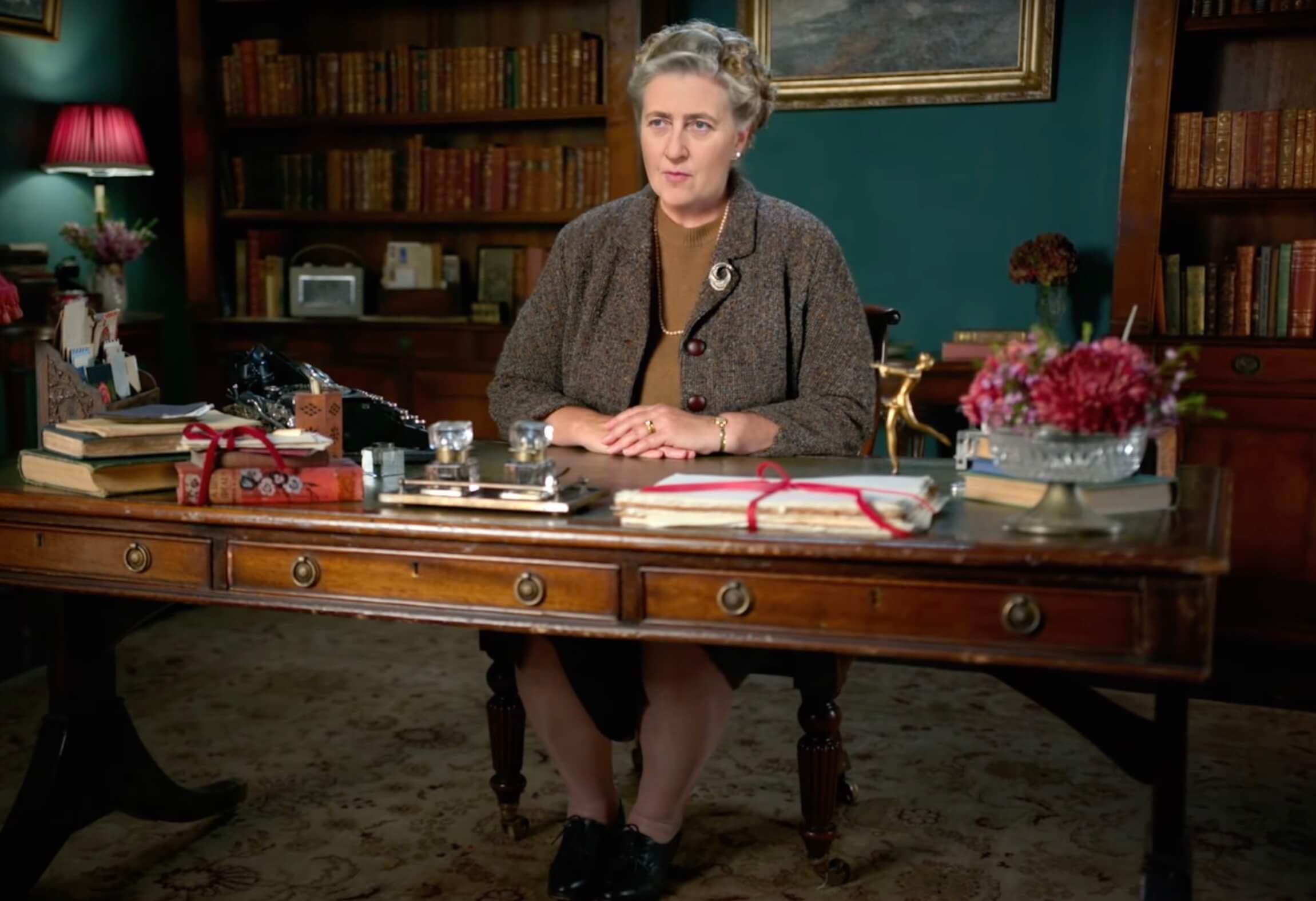 AI-enhanced actor playing Agatha Christie, seated at a desk in a period room 