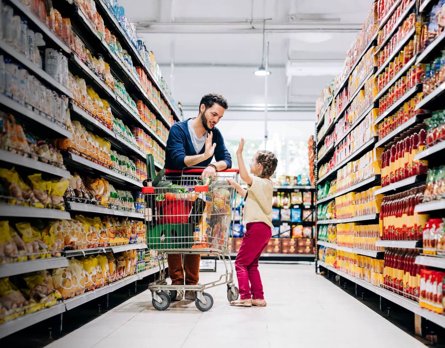 An adult giving a child a high five in a supermarket aisle 
