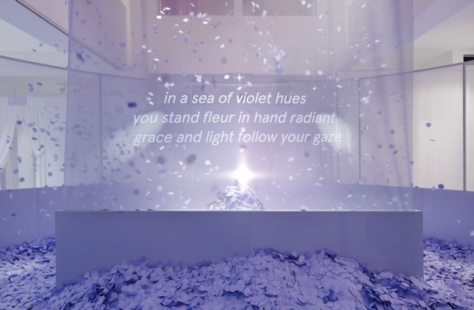 Purple confetti falling around a gauzy panel with a poetic text: 'in a sea of violet hues, you stand fleur in hand'  