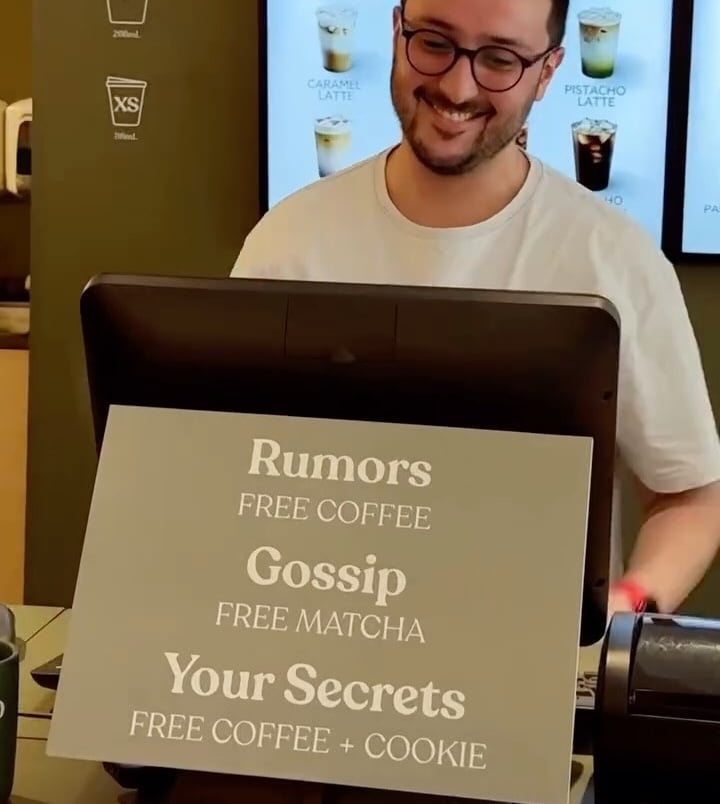 Employee at cash register with sign promoting free beverages for gossip and secrets 