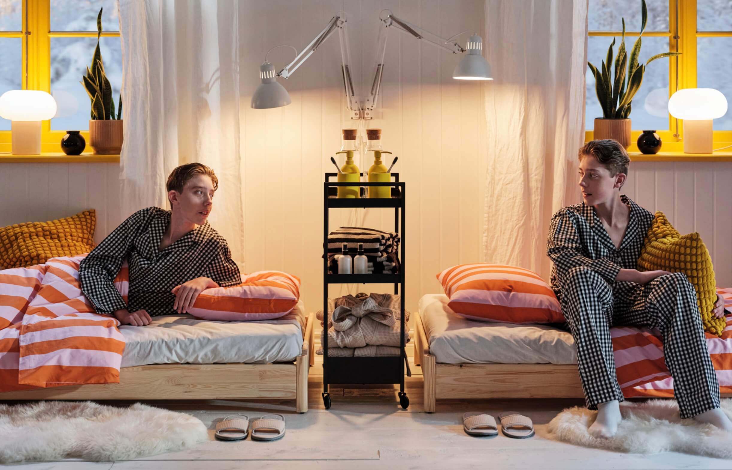 Identical young adult twins in matching pajamas on their beds, glancing at each other 