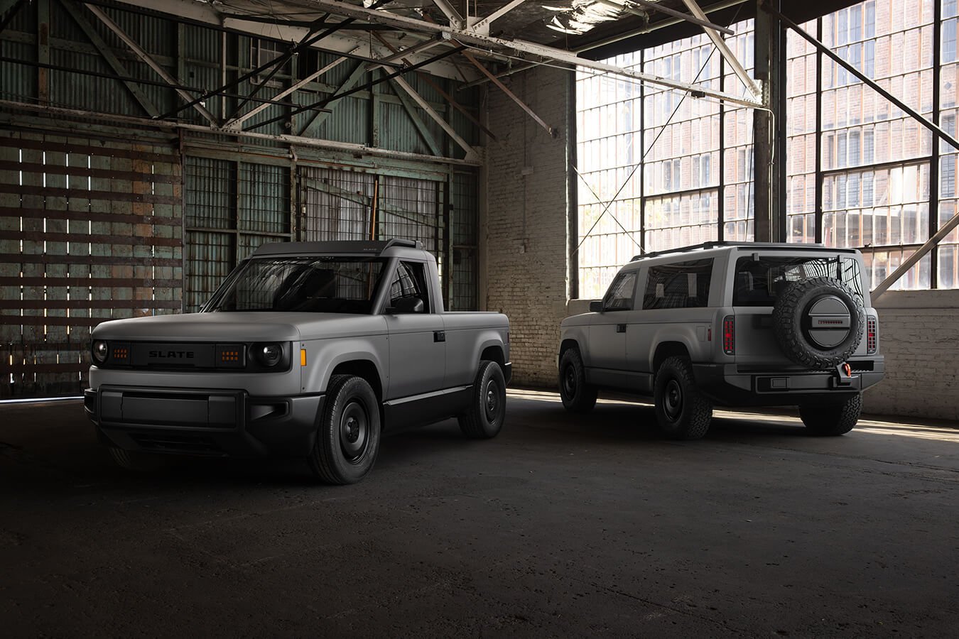 Two versions of the Slate truck, a pickup and an SUV, parked in an industrial building 