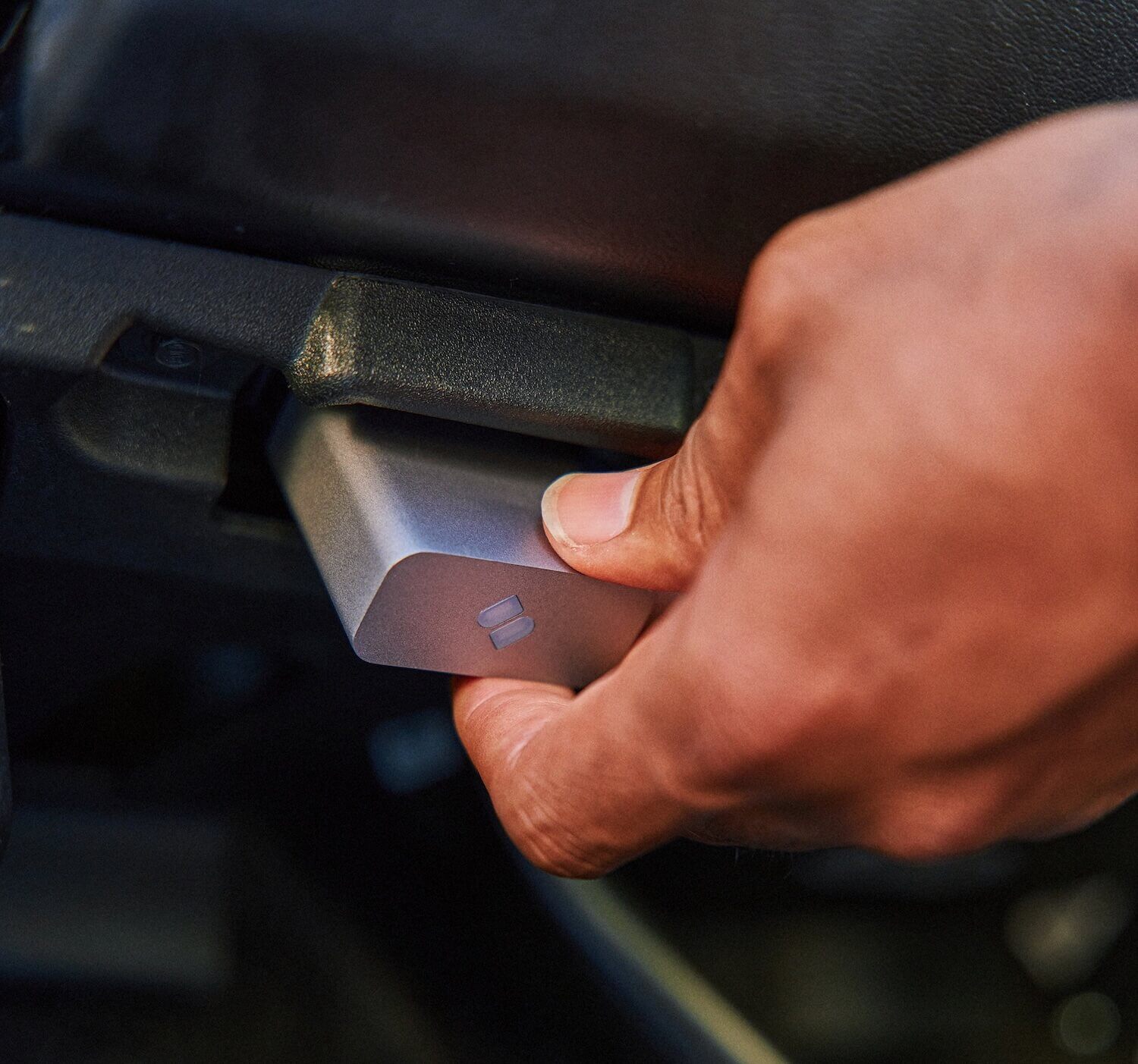 Hand inserting a compact, silver-colored Sparq device into a vehicle's OBD-II port 