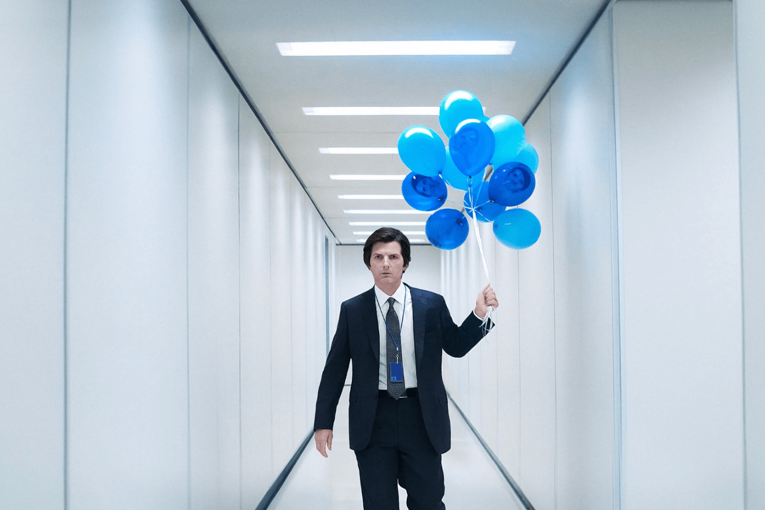Adam Scott in Severance, walking down a white corridor holding blue balloons 