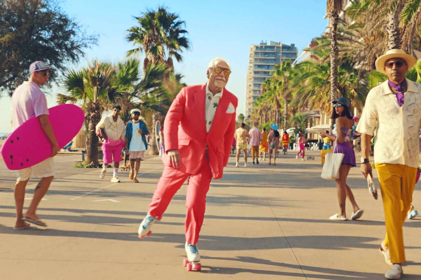 Actor Brian Cox wearing a pink suit and roller-skating down a beachside boulevard 